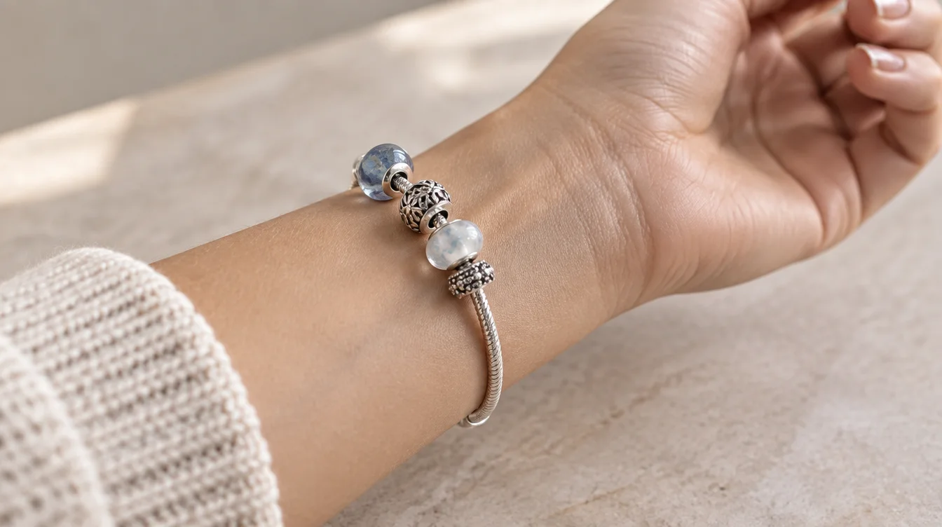 A partly filled bead charm bracelet on a wrist, with bare carrier visible beside glass and metal beads.